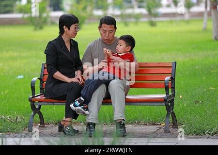 Contea di Luannan, Cina - 13 giugno 2023: La famiglia riposa su una panchina del parco, Cina settentrionale Foto Stock