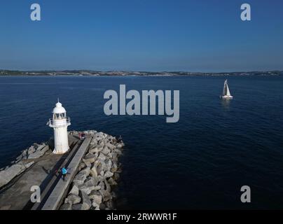 Brixham, Torbay, South Devon, Inghilterra: VISTA DRONI: Faro e muro di Brixham Harbour; yacht diretto verso il mare. Brixham è un popolare resort di villeggiatura nel Regno Unito Foto Stock