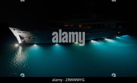 Yacht a motore di lusso, splendide luci sottomarine che illuminano le acque blu turchesi di Cavtat Bay, Croazia. Illuminazione sott'acqua Foto Stock