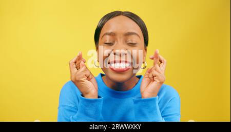 Bella giovane donna con le dita incrociate, desiderosa e sperante, studio giallo Foto Stock
