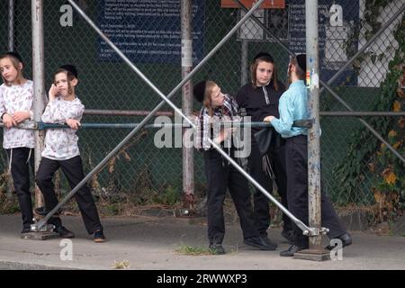 I ragazzi ebrei ortodossi con un lungo peyot aspettano di essere prelevati dal loro scuolabus. All'angolo di una strada a Williamsburg, Brooklyn, New York. Foto Stock