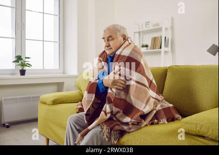 Ritratto di un uomo anziano che cerca di tenersi al caldo sotto una coperta a casa. Foto Stock
