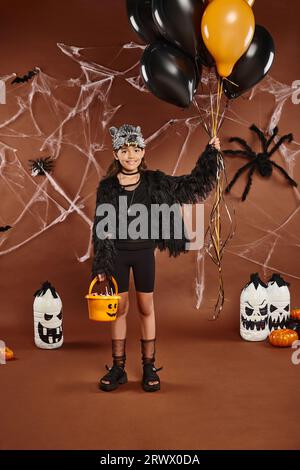 smiley Girl tiene palloncini neri e arancioni e un secchiello con dolci, concetto di Halloween Foto Stock