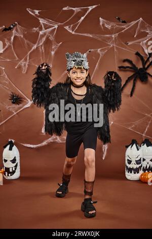 smiley preteen girl che spaventa e posa in abiti in pelliccia sintetica con maschera lupo, concetto di Halloween Foto Stock