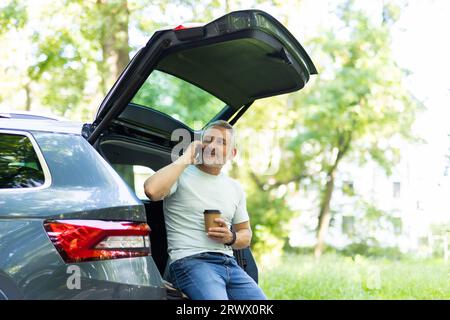 Un giovane viaggiatore seduto nel bagagliaio parla al telefono Foto Stock