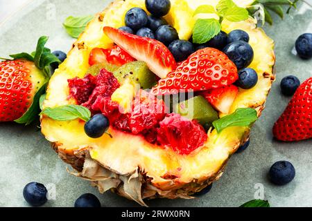 Gustosa insalata estiva di fragole, kiwi, frutti di bosco e arancia in mezzo ananas. Primo piano Foto Stock