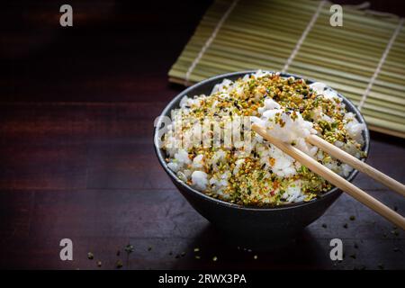 Primo piano di riso con spezie giapponesi in ciotola nera e bacchette su sfondo di legno, spazio per la copia, cibo asiatico tradizionale, Foto Stock