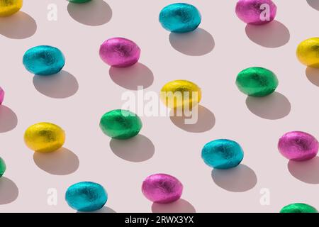 Elegante motivo piatto senza cuciture di uova di alluminio multicolore su sfondo rosa pastello concetto pasquale minimalista. Foto Stock