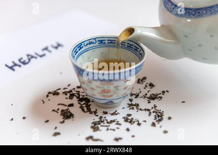 Una teiera che versa una tazza di tè verde con foglie di tè isolate in bianco. Bevanda salutare e concetto di stile di vita sano. Foto Stock