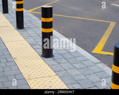 Pavimentazione tattile gialla per la tendina alla fermata dell'autobus. Fermata dell'autobus con dissuasori stradali che proteggono il marciapiede pedonale. Limitazione del traffico concettuale Foto Stock