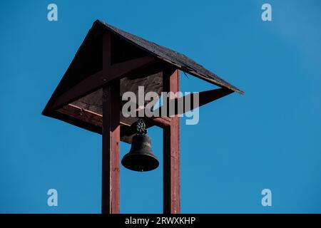 Helsinki / Finlandia - 18 SETTEMBRE 2023: Primo piano di un vecchio palo di legno con una campana contro un cielo blu brillante Foto Stock