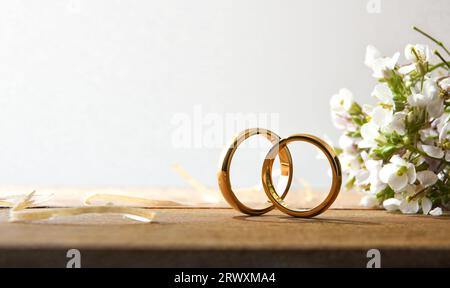 Dettaglio di due anelli d'oro su un tavolo rustico in legno con bouquet di fiori e sfondo bianco isolato. Vista frontale. Foto Stock