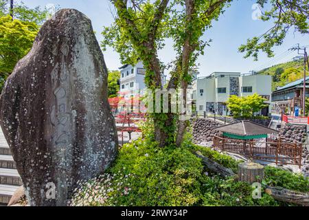 Monumento in pietra di Shuzenji Onsen Tokko no Yu Park e Tokko no Yu sulla riva opposta Foto Stock