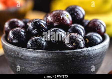 Jaboticaba o jabuticaba, frutti brasiliani e sudamericani, in una pentola di argilla con frutti tropicali sullo sfondo. Foto Stock