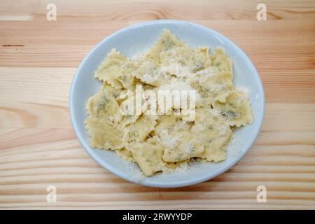Vista dall'alto e ravvicinata a Ravioli sulla sommità con parmigiano, sul tavolo di legno. Foto Stock