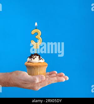 Dolce di compleanno consegnato a mano - candela numero 3 su sfondo blu Foto Stock