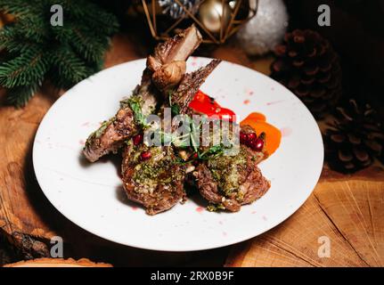 Costolette di agnello arrosto con erbe, semi di melograno e peperoni grigliati su un piatto bianco. Cibo di Natale. Foto Stock