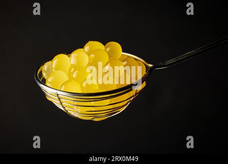 palle di gelatina gialle per preparare il tè a bolle in una succhieruola su sfondo nero Foto Stock