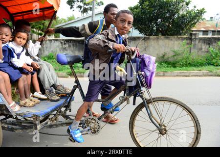 I bambini della scuola elementare malgascia vanno a scuola in risciò ciclistico a Moramanga, Madagascar. Foto Stock