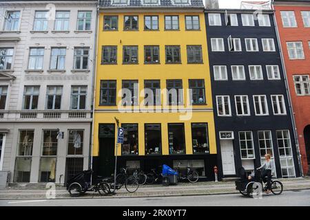 Una donna danese che pedala di fronte a un edificio colorato lungo Gammel Mønt nel centro di Copenaghen, Danimarca. Foto Stock