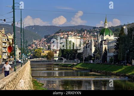 Vista del Ponte Festina lente e dell'Accademia di Belle Arti dalle rive del fiume Miljacka che separarono le due sponde nella guerra in Bosnia Foto Stock