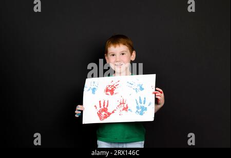 le impronte del bambino su un foglio bianco di carta mentre disegnare con le mani del bambino utilizzando vernici multicolore Foto Stock