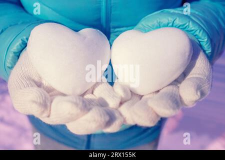 Due palle di neve a forma di cuore nelle mani femminili in inverno Foto Stock