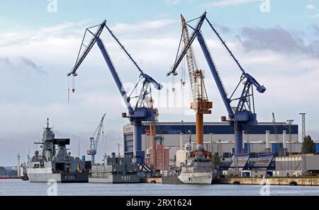 22 settembre 2023, Meclemburgo-Pomerania occidentale, Warnemünde: La fregata "Hessen" (l-r), la nave residenziale "Knurrhahn" e una nave da caccia minata sono ormeggiate nell'arsenale navale. La fregata è ormeggiata la mattina presto ed è prevista una nuova navigazione nel pomeriggio dopo una breve sosta di manutenzione. Il governo tedesco ha acquistato il cantiere navale Warnow nell'estate del 2022 in seguito all'insolvenza del gruppo MV Shipyards. L'arsenale navale ripara quattro navi navali all'anno, come previsto. Foto: Bernd Wüstneck/dpa Foto Stock