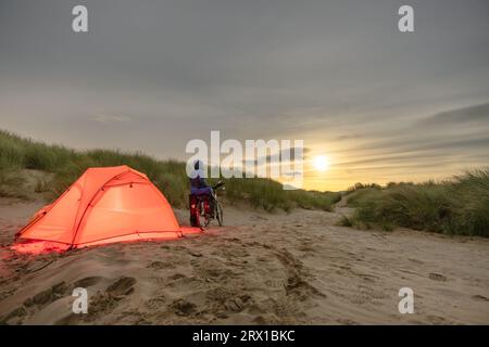 Uomo con bicicletta Touring Camping sulla spiaggia sotto la Luna piena Foto Stock
