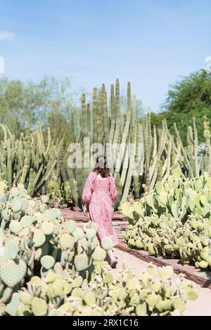 Una donna in maxi abito rosa floreale che cammina attraverso i cactus del deserto Foto Stock