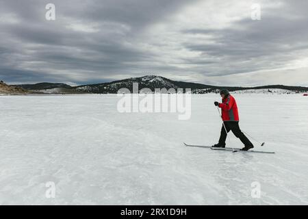 L'uomo attraversa il cielo di fondo attraverso il lago ghiacciato in montagna Foto Stock