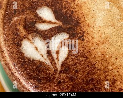 Vista ravvicinata dall'alto delle decorazioni e dei vortici realizzati con un cappuccino. Spruzzi di cioccolato visibili Foto Stock