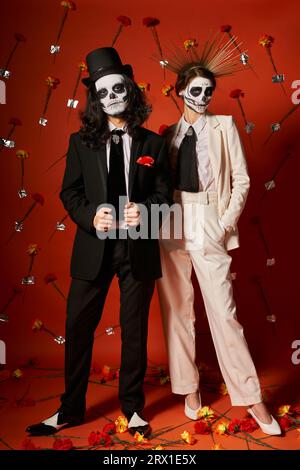 elegante coppia nel trucco dia de los muertos su sfondo rosso con decorazioni floreali Foto Stock