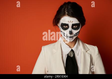 donna spaventosa nel trucco e nell'abbigliamento festivo di catrina calavera che guarda la macchina fotografica su un ritratto rosso Foto Stock