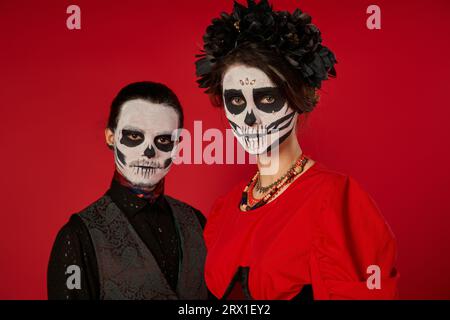 coppia inquietante nel tradizionale trucco catrina guardando la macchina fotografica sul rosso, festa dia de los muertos Foto Stock