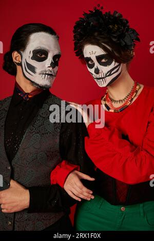 coppia spaventosa nel trucco catrina calavera guardando la macchina fotografica sul rosso, la tradizione dia de los muertos Foto Stock