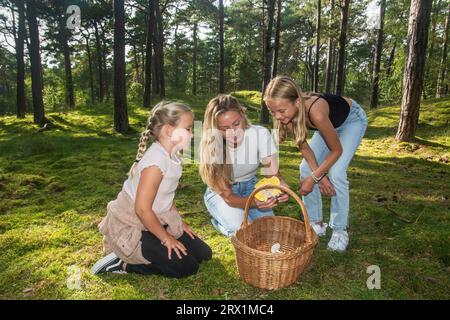 Donna bionda con due ragazze, 7 e 10 anni, alla ricerca di funghi nella foresta di Ystad, Scania, Svezia, Scandinavia Foto Stock