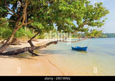 Scenografica spiaggia di sabbia bianca remota sull'isola tropicale della Thailandia, piccola barca e altalena attaccata a un albero Foto Stock