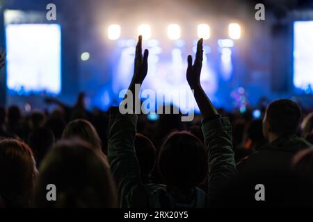 Esibizione di band rock in un concerto in un nightclub. La folla della fila anteriore sta festeggiando. Sagome di ventole stringi le mani davanti al labbro Strobing colorato e luminoso Foto Stock