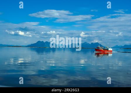 Barca da pesca rossa che naviga sull'acqua con montagne in lontananza vicino a Svolvaer in Norvegia Foto Stock