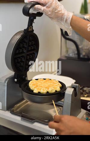 il cuoco controlla l'impasto per i waffle dolci nel ferro da stiro con un bastoncino di legno Foto Stock