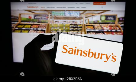 Persona che possiede uno smartphone con il logo dell'azienda britannica di supermercati J Sainsbury plc sullo schermo di fronte al sito Web. Concentrarsi sul display del telefono. Foto Stock