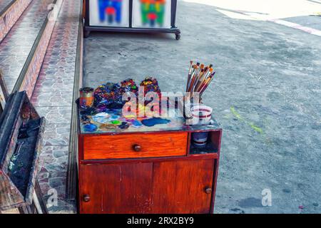 Attrezzature per artisti di strada. Vecchio tavolo in legno, pennelli, tavolozza e pitture secche sulla strada della città. Studio di pittura in strada cittadina Foto Stock