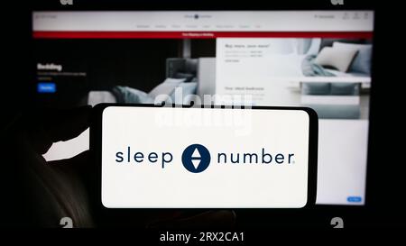 Persona che tiene uno smartphone con il logo della società statunitense Sleep Number Corporation sullo schermo davanti al sito Web. Concentrarsi sul display del telefono. Foto Stock