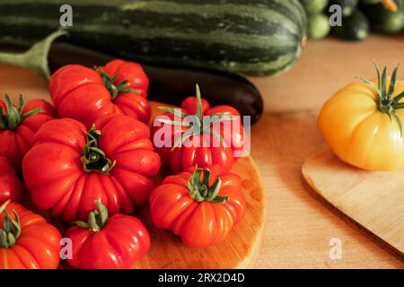 Pomodori grandi maturi, melanzane, verdure su un locale di lavoro in legno della cucina. Molte verdure crude di fondo. Pomodoro, cetrioli. Fornello a casa che fa una h Foto Stock