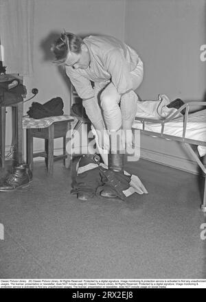 I vigili del fuoco negli anni '1940 Un vigile del fuoco viene svegliato dall'allarme che suona in una stazione dei vigili del fuoco a Kungsholmen a Stoccolma, e deve essere veloce vestirsi e scappare con il camion dei pompieri per iniziare il lavoro di estinzione. Le sue scarpe e i suoi pantaloni sono pronti a entrare per vestirsi rapidamente. Svezia, febbraio 1940. Kristoffersson rif. 57-8 Foto Stock