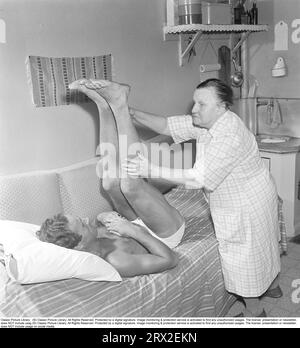 Massaggio negli anni '1950 Una donna anziana dà a un uomo più giovane, che è sdraiato su un letto, un trattamento sotto forma di massaggio e stretching. Svezia 1954. Kristoffersson rif. BM9-3 Foto Stock