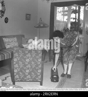 Aspirare negli anni '1940 Una donna in casa ha finito di aspirare il salotto, ha il cavo in una mano e afferra l'aspirapolvere con l'altra per continuare a aspirare la stanza successiva. La camera è arredata con mobili d'epoca degli anni '1940, un divano e un paio di poltrone intorno ad un tavolo. Nell'angolo c'è una piantana. Svezia 1947. Kristoffersson rif. V96-6 Foto Stock