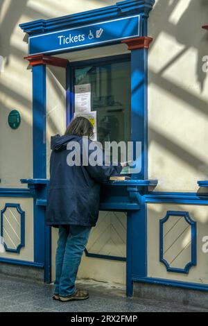 Donna che acquista i biglietti del treno o fa una richiesta presso la biglietteria della stazione ferroviaria di King's Lynn. Foto Stock