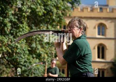 Il giardiniere della Trinity Dr Jo Miles affina la sua falce prima di falciare fiori selvatici nel Meadow Circle presso il XIX secolo New Court del Trinity College di Cambridge. La falciatura, o falciatura, è una tradizione secolare che si ritiene sia stata praticata a Trinity prima dei rasaerba. Data immagine: Venerdì 22 settembre 2023. Foto Stock